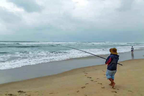 Рыбак рыбалка в океане с пляжа на закате — стоковое фото