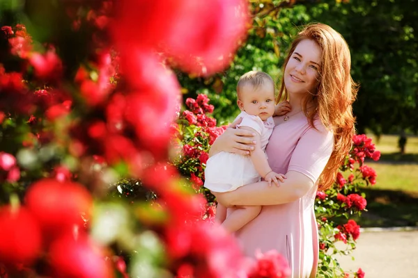 在玫瑰园里有个女婴的年轻女子 — 图库照片