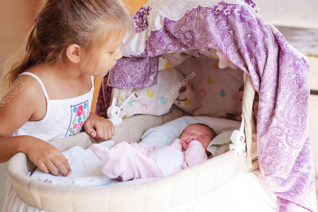 little girl looking at the newborn baby in crib