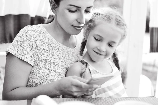 Glückliche Mutter Und Kleine Tochter Mit Smartphone Café lizenzfreie Stockbilder