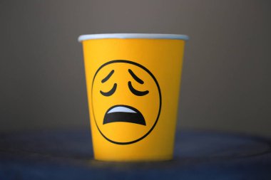 Kağıt bardakta hüzünlü duygu emojisi. Sıkıcı ofis işleri..