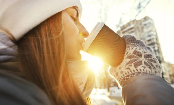 Young woman drinks coffee from the paper cup in the winter park