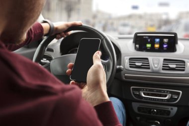 Arabasının direksiyonuna oturan ve elinde telefonuna arayan genç adam