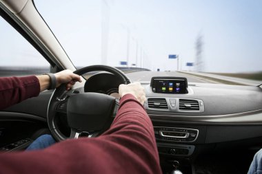 Genç adam asfalt yolda modern arabayı kullanıyor.