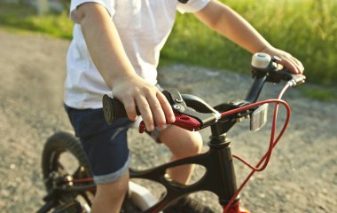 Küçük çocuk asfalt yolda bisiklete biniyor.