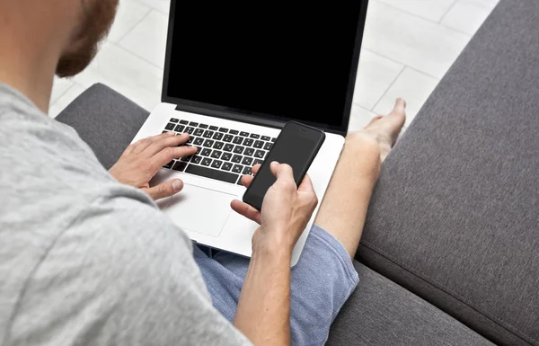 Ο νεαρός άντρας κάθεται στον καναπέ και δουλεύει με φορητό υπολογιστή — Φωτογραφία Αρχείου