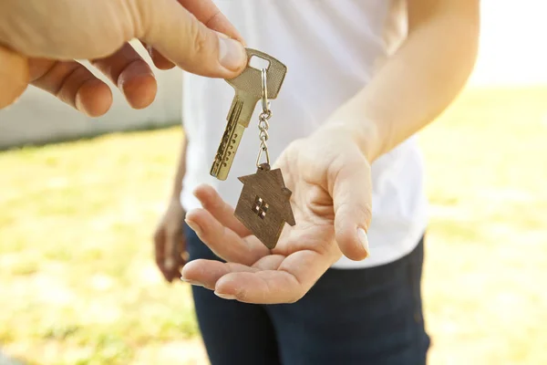 Man giving the metal key from door with wooden trinket in shape — Stock Photo, Image