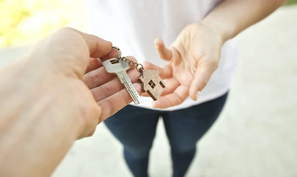 Человек дает металлический ключ от двери с деревянной безделушкой в форме — стоковое фото