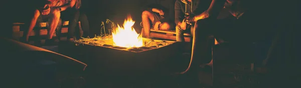 De groep vrienden zitten in de buurt van de vreugdevuur in de nacht een — Stockfoto