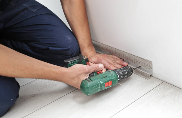 Хозяин устанавливает пластиковый плинтус в доме
