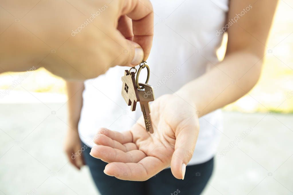 Man giving the metal key from door with wooden trinket in shape 