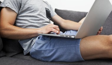 Genç adam kanepede oturuyor ve dizüstü bilgisayar la çalışıyor.