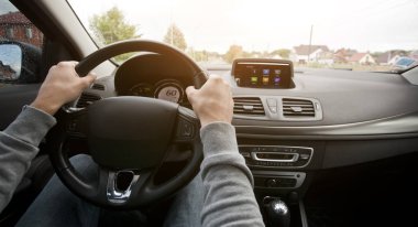 Genç adam asfalt yolda modern arabayı kullanıyor.