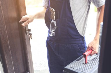 Tamirci elinde alet çantasıyla eve geliyor.