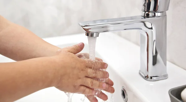 El chico se lava las manos con jabón bajo el agua. —  Fotos de Stock