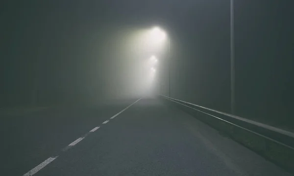 La espesa niebla sobre el camino de asfalto en la noche fuera de la ci — Foto de Stock