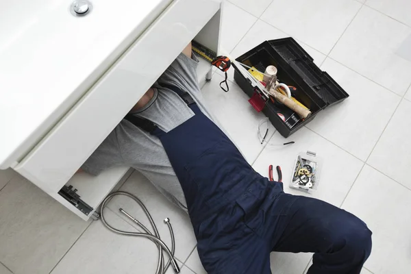 The young repairer is fixing sink in the bathroom — Stock Photo, Image