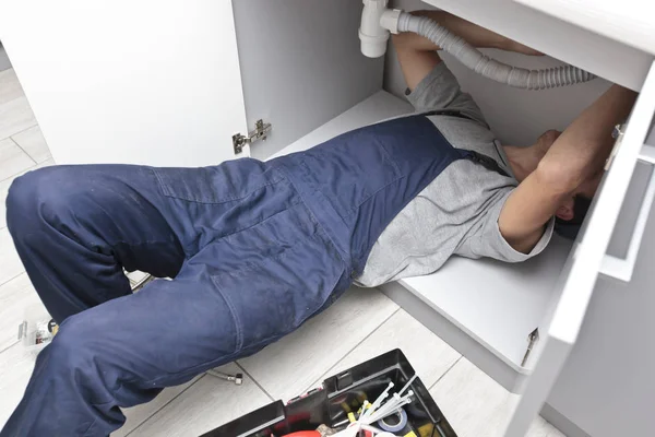 The young repairer is fixing sink in the kitchen Royalty Free Stock Images