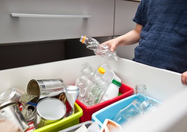 Çocuk, çöpleri ayıklamak için dört farklı çöp kutusundan birine plastik çöp atıyor.. 