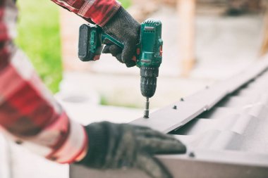 Çatıdaki metali vidalayan çatı işçisi.