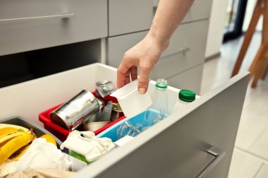 Kadın dört konteynırdan birine plastik konteynır atıyor ya da çöpü ayırıyor.