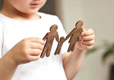 Anne, baba ve çocuğun tahta figürlerine bakan küçük çocuk. Aile hayali kuran çocuk konsepti