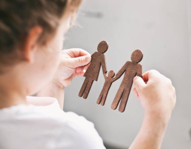 Anne, baba ve çocuğun tahta figürlerine bakan küçük çocuk. Aile hayali kuran çocuk konsepti