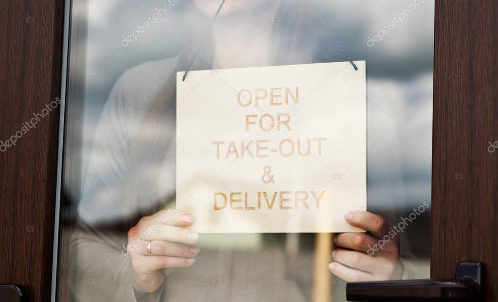 Woman holds the wooden sign with text: Open for take-out and delivery