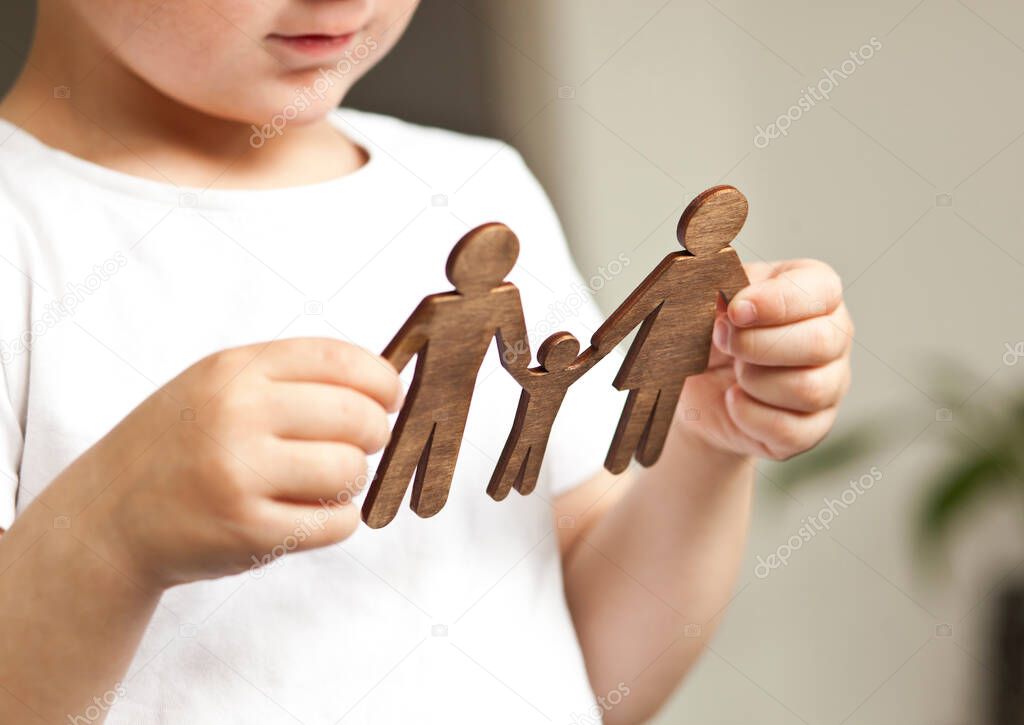 The little child looking on the wooden figures of mom, dad and child in his hands. Concept of the child dreaming about family