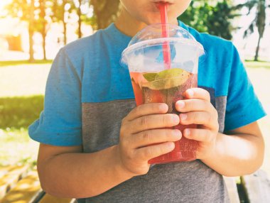 Çocuk plastik bardaktaki pembe limonatayı içiyor.