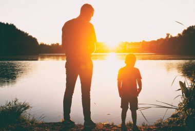 İki kardeş gün batımında gölün kıyısında duruyorlar.