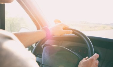 Genç adam asfalt yolda modern arabayı kullanıyor.