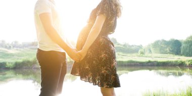 Mutlu hamile çift ve göl kenarında gün batımında