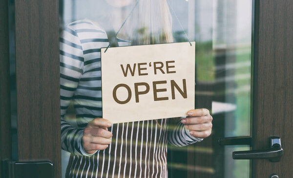 Женщина держит деревянный знак с текстом: мы открыты
 