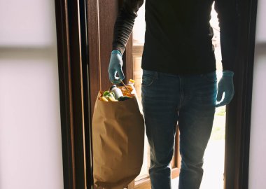 Adam marketten aldığı çantayla eve geliyor ve eldiven takıyor.