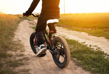 Küçük çocuk akşam kırsal yolda bisiklet sürüyor.