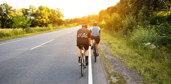 两名骑单车者日落时穿过柏油路 — 图库照片