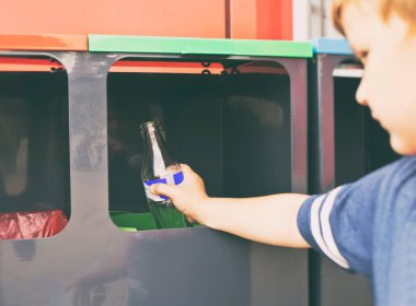 Çocuk, cam şişeyi çöpleri ayırmak için dört kutudan birine atıyor.