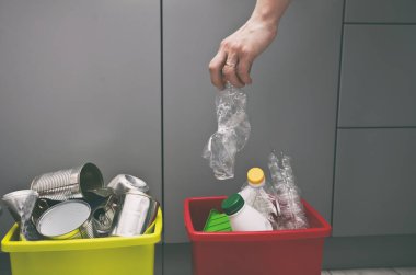 Kadın dört konteynırdan birine plastik şişe atar ya da çöpü ayırır.