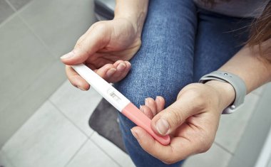 Kadın banyodaki hamilelik testini kontrol ediyor.