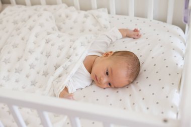 Smiling 2-3 month old baby lying on white bedding with soft fleece blanket, showing happy mood in the morning