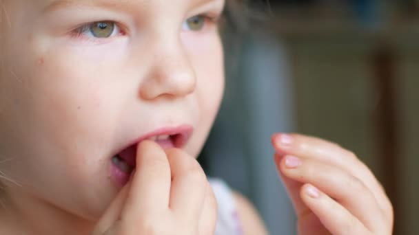 Plan d'un enfant léchant de la nourriture de son doigt. Puis elle se retourne et sourit . — Video