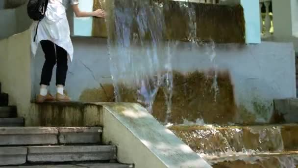 Junge Frau fängt einen Tropfen aus einem Brunnen. — Stockvideo