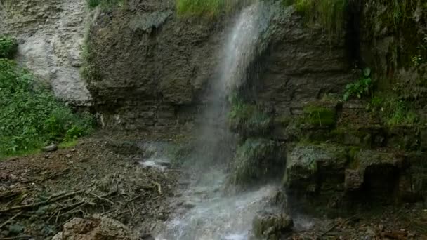 Tiro backup de uma longa e fina cachoeira como ele derrama para baixo do lado de um penhasco rochoso e musgoso — Vídeo de Stock