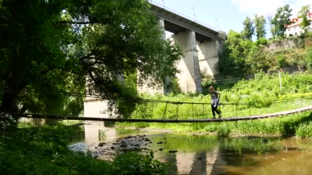 Fille voyageuse debout sur un pont à travers une rivière de montagne — Video