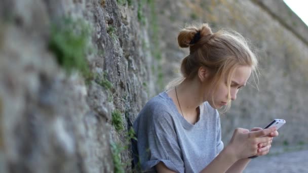 Rödhårig flicka skriver ett meddelande som lutar mot en stenmur. — Stockvideo