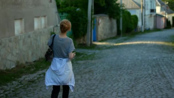 Frau, die im Freien durch die herbstliche Stadtstraße läuft. 4k. junge Frau beim Spazierengehen mit Smartphone. Herbstabend — Stockvideo
