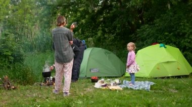 Akşam aile kampı. Mutlu anne, baba ve kızı çadırın oturuyor. Kırsal kesimde tatil