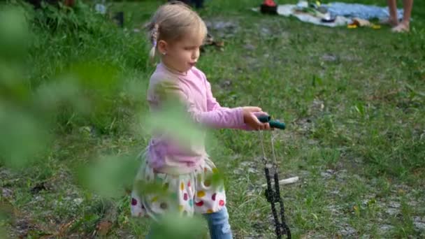 Una niña preescolar con una sierra turística en las manos trata de cortar madera en el bosque — Vídeos de Stock