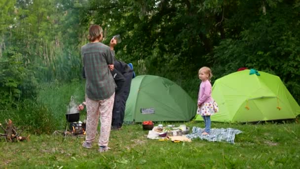 Boa noite, no acampamento da família. Mãe feliz, pai e filha sentados perto da tenda. Férias no campo — Vídeo de Stock